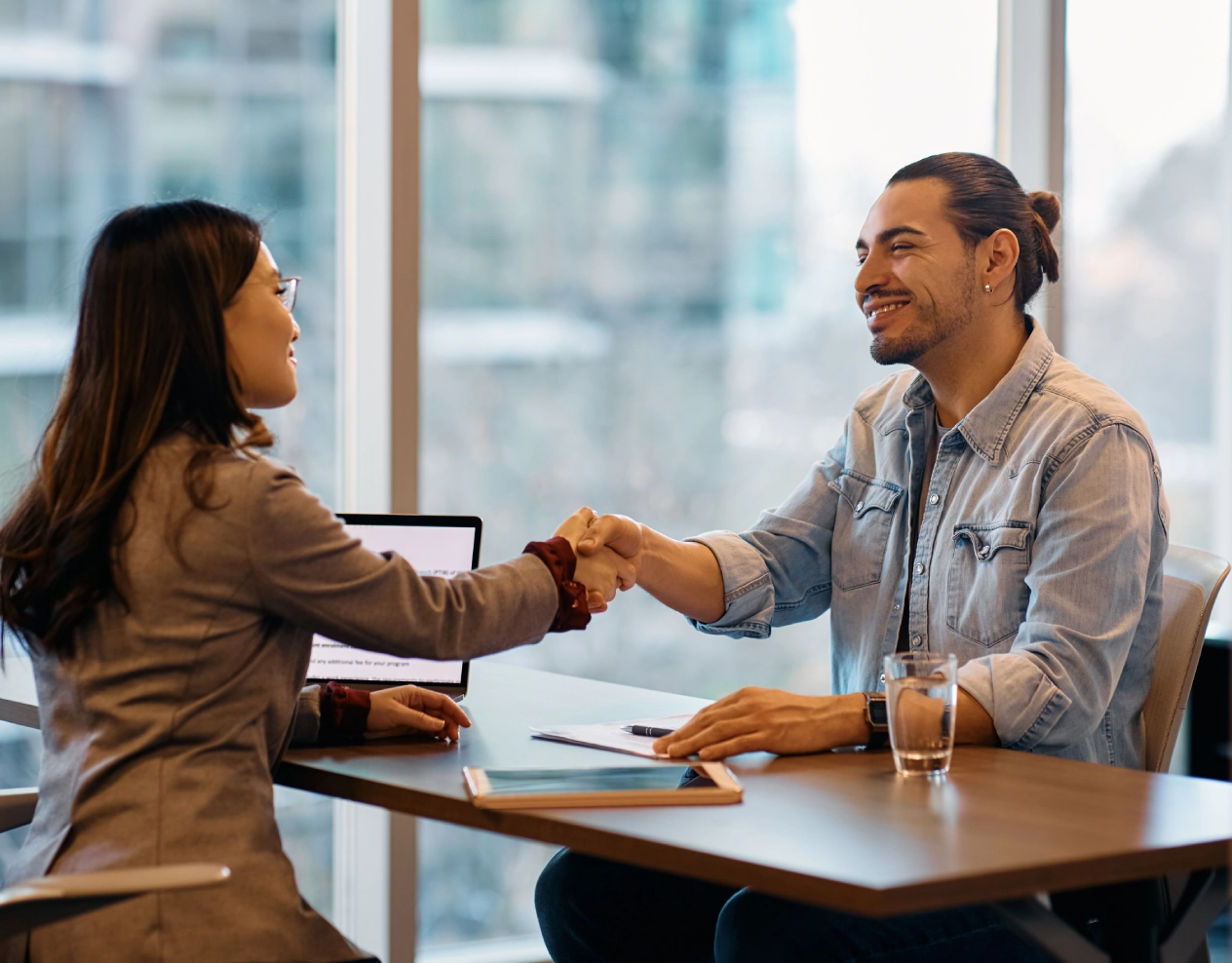 A man and woman shaking hands over a table.